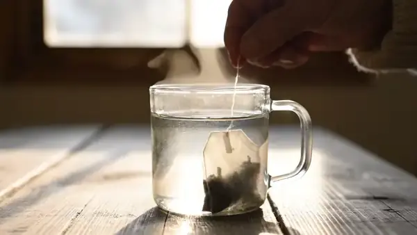 Red and amber color swirling out of a tea bag into a clear glass mug of hot water